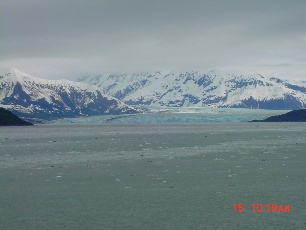 Auto-generated description: A vast, icy body of water stretches out towards snow-covered mountains under a cloudy sky.